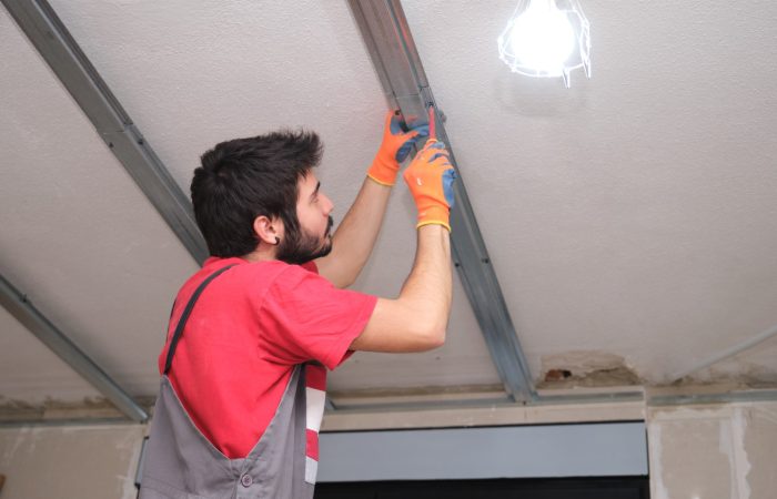 Construction worker assembling a suspended ceiling metal frame with a screwdriver.